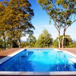 Inground swimming pool with wooden deck and glass fence