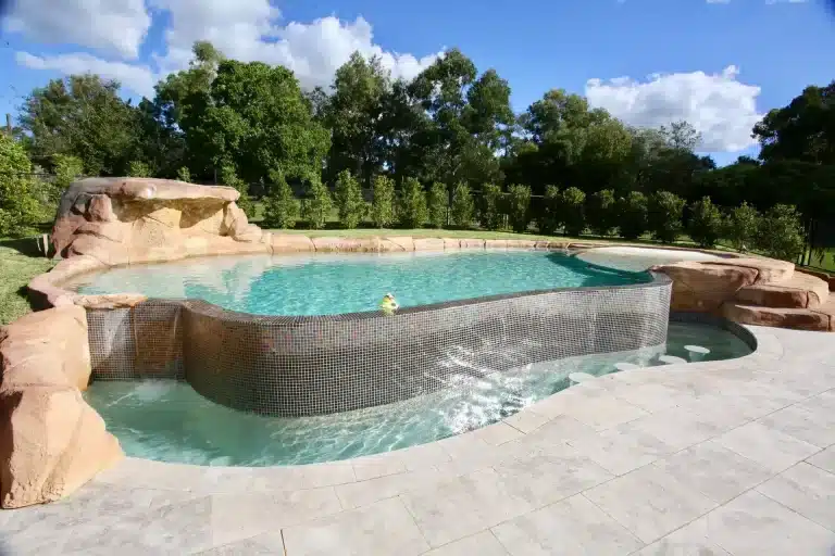 Luxury Above Ground Concrete Pool with lagoon-style design, rock features, and an elevated spa in a natural backyard setting
