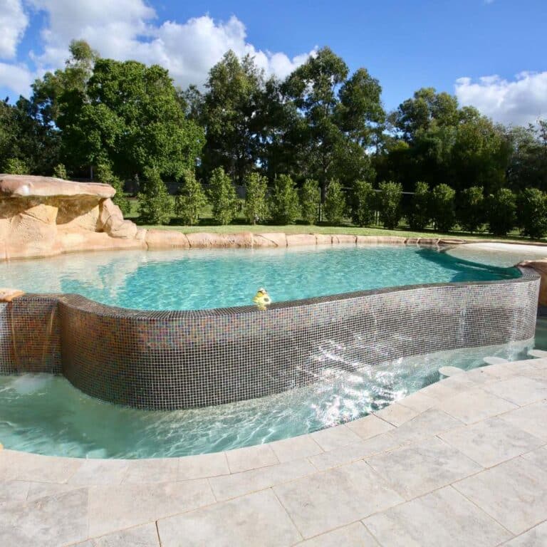 Above Ground Concrete Pool by Blue Haven Pools surrounded by natural stone landscaping