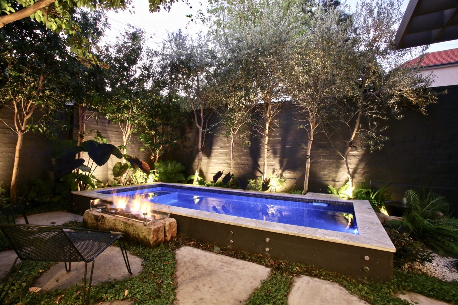 Luxury concrete pool at night surrounded by landscaped garden in Bondi Junction, built by Blue Haven Pools