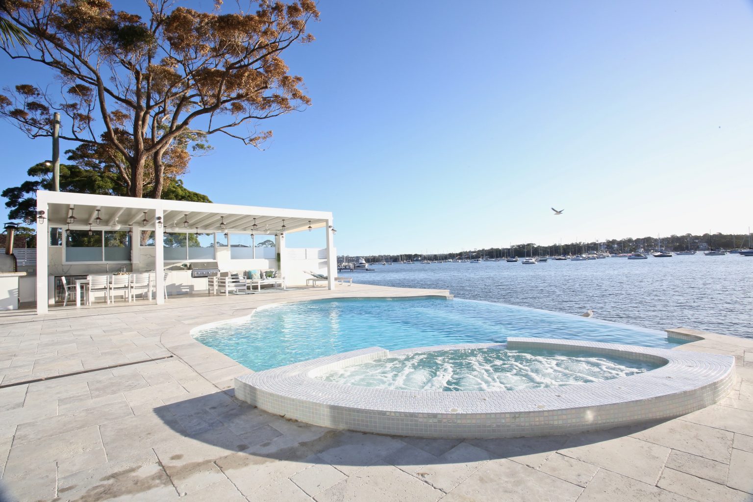 Modern outdoor living space with concrete pool, raised spa, cabana and waterfront entertaining design