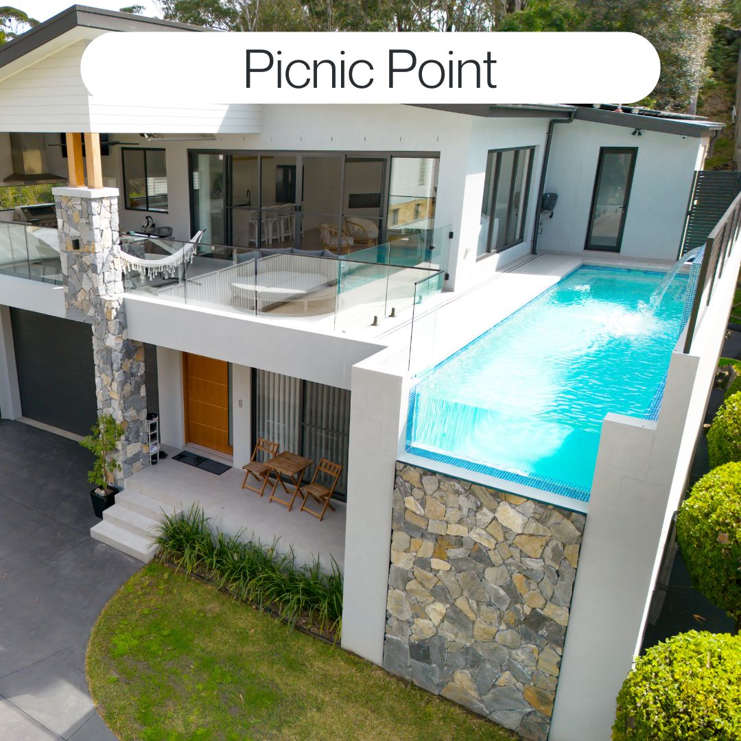 Elevated custom concrete pool in Picnic Point with wet edge design, stone feature wall, glass fencing and modern home integration