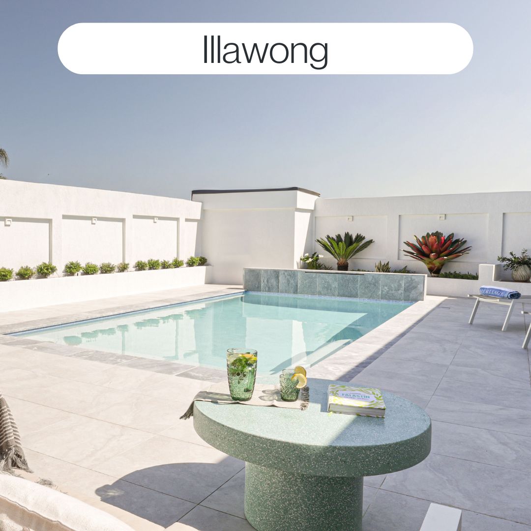Modern backyard swimming pool in Illawong with tiled feature wall, white paving, landscaped surrounds and contemporary outdoor design