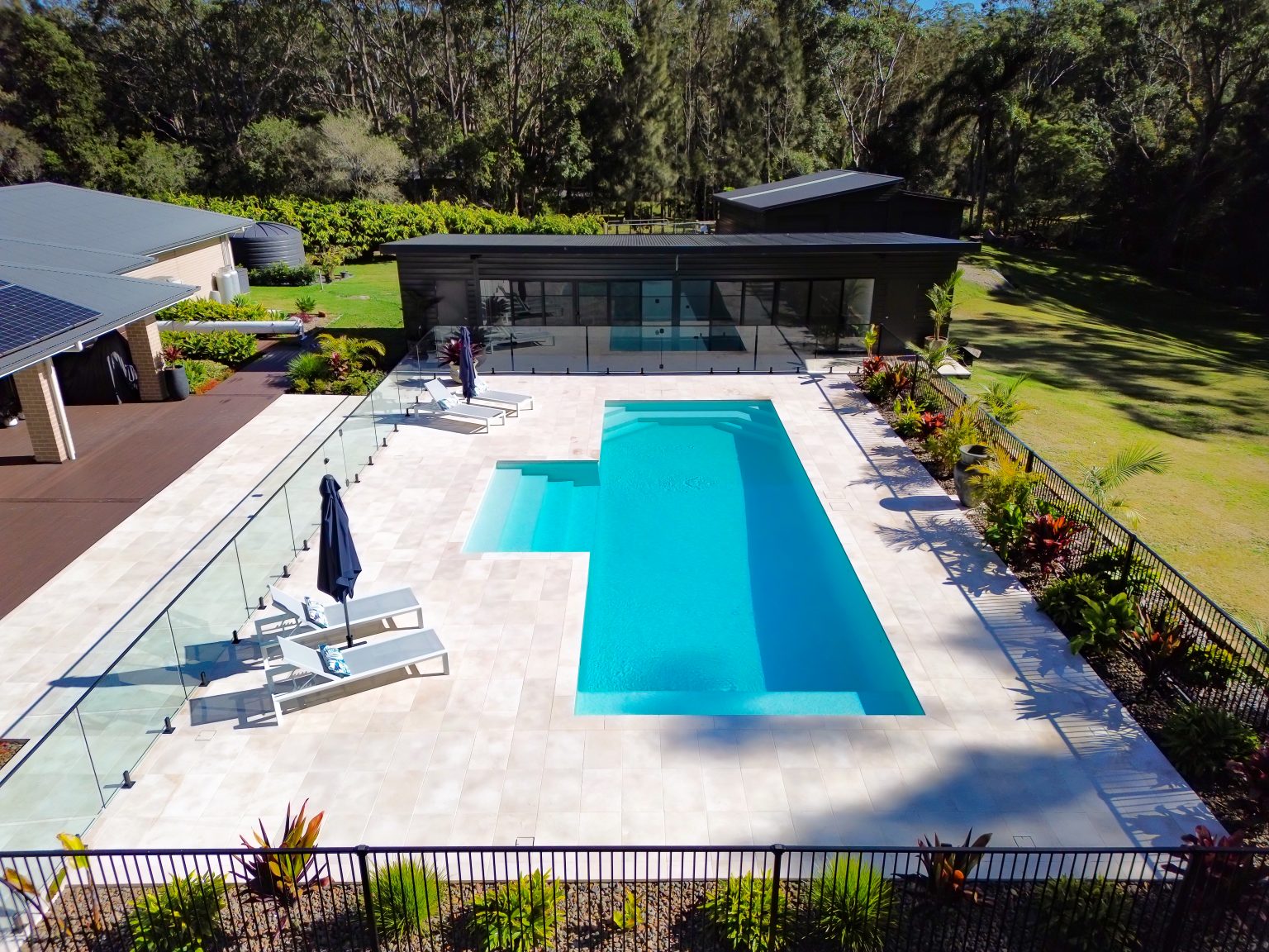 Shallow relaxation ledge in 12m concrete backyard pool designed for resort style outdoor living