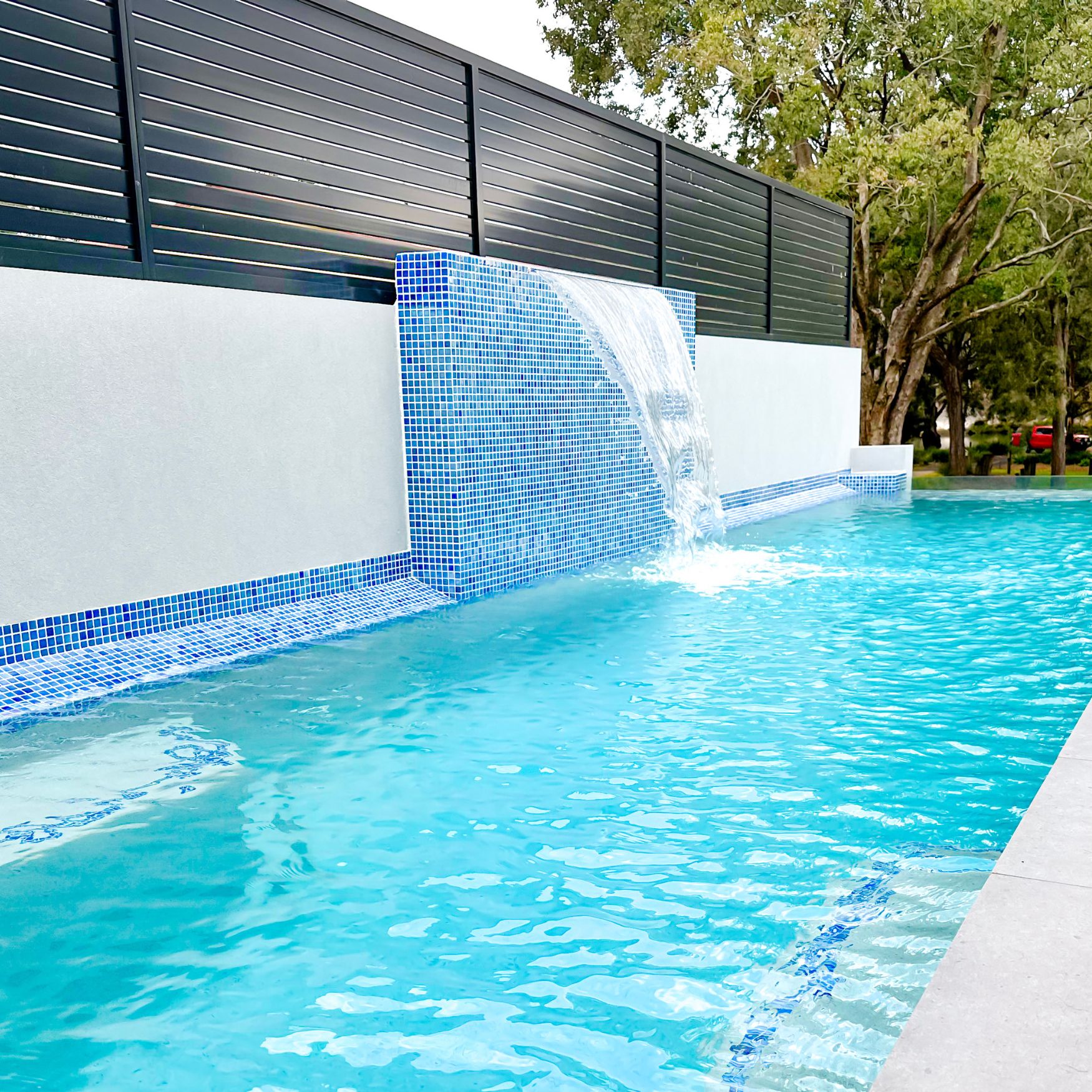 Raised pool feature wall and sheer descent waterfall at The Glassline pool project in Picnic Point